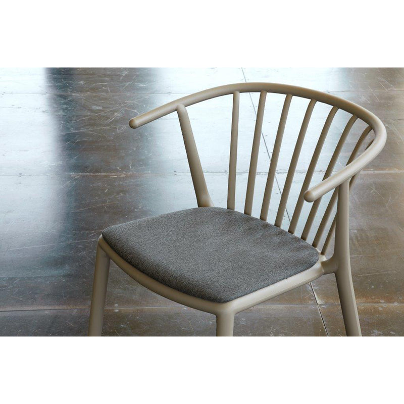 The Woody Upholstered Chair by Resol has a light beige wooden frame, a curved backrest with vertical slats, a cushioned gray seat, crafted sustainably, and placed on a polished stone floor.