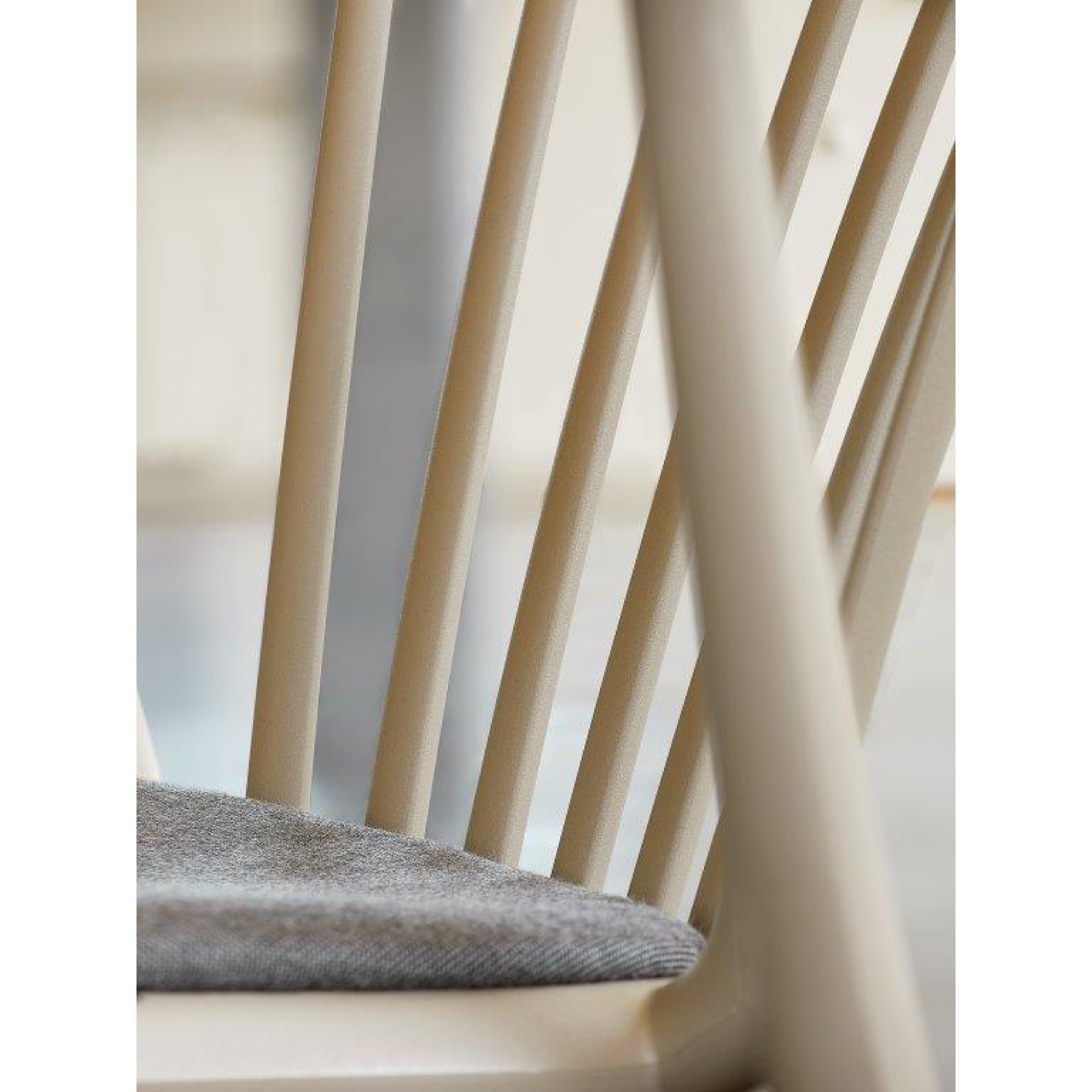 Close-up of the Woody Upholstered Chair by Resol, showcasing beige vertical slats and a soft gray cushion. The blurred background highlights the chairs modern design, smooth texture, and sustainable production.