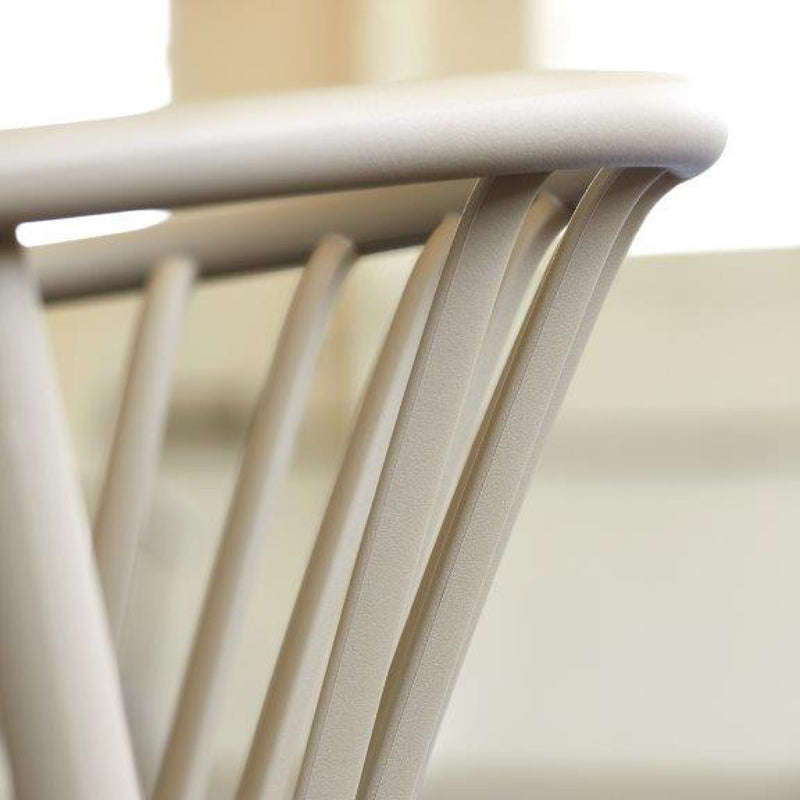 Close-up of the Woody Upholstered Chair by Resol, featuring slender, curved vertical rods on its beige back. The smooth finish stands out against a softly blurred background, highlighting the chairs design for interior furniture.
