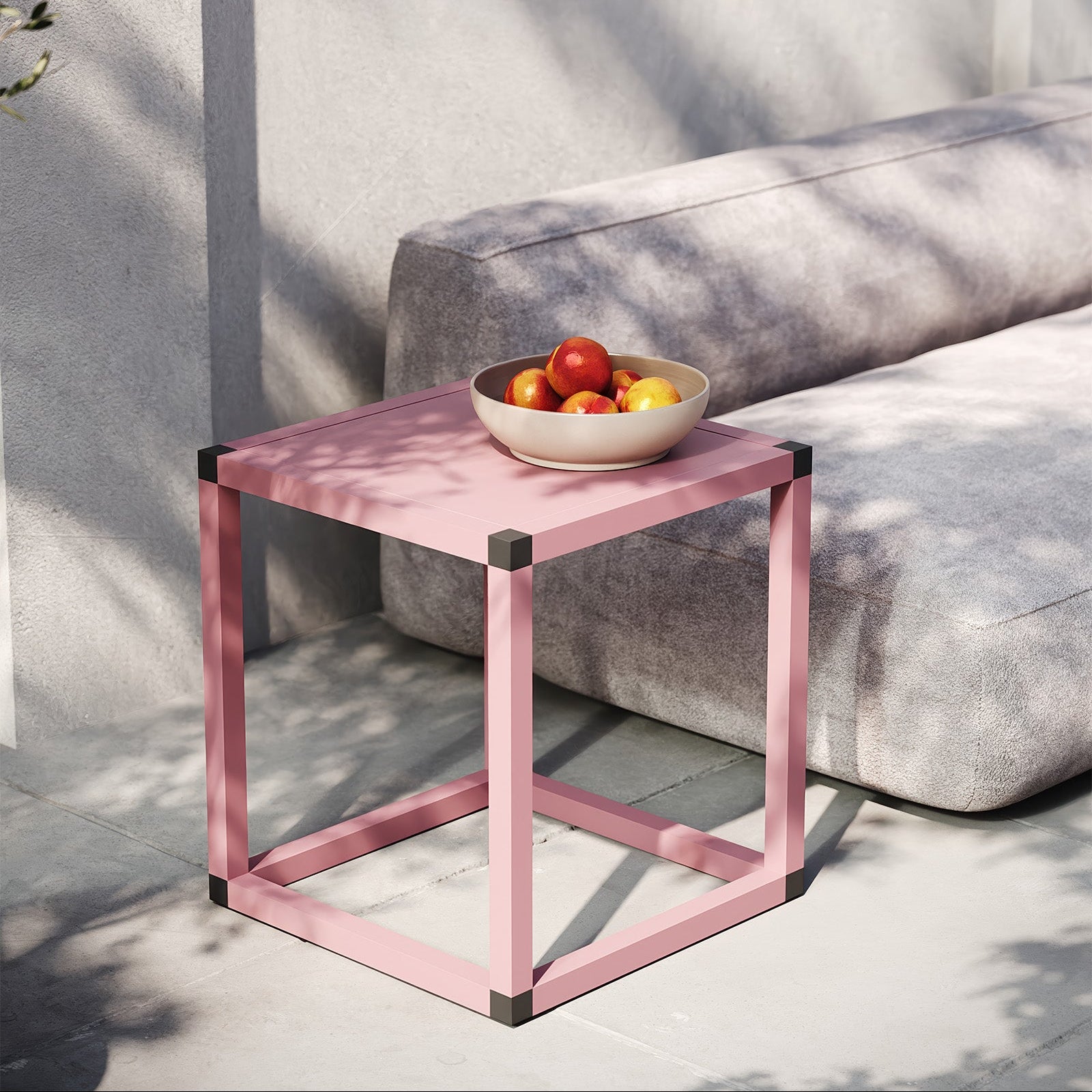 Pink side table with a bowl of fruit on a gray sofa outdoors.