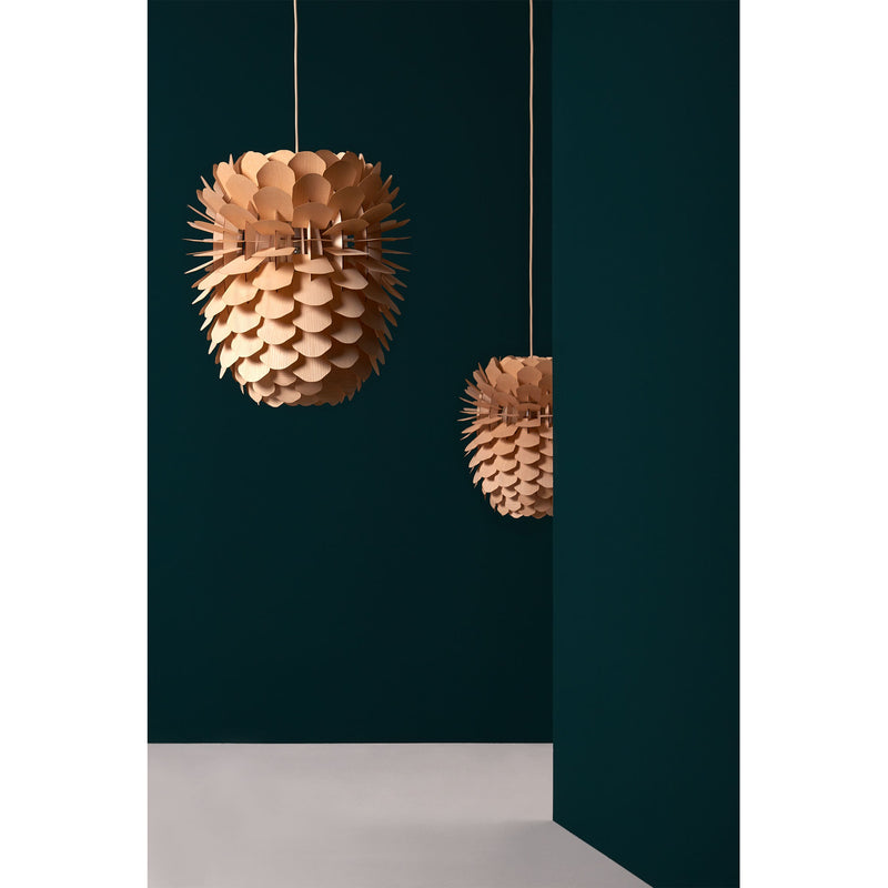 Two Zappy Ash lamps by Schneid, featuring a spiky wooden design with oak veneer, hang against a dark teal wall. The foreground reveals part of a white floor and the corner of another teal wall, exuding a minimalist and modern aesthetic.