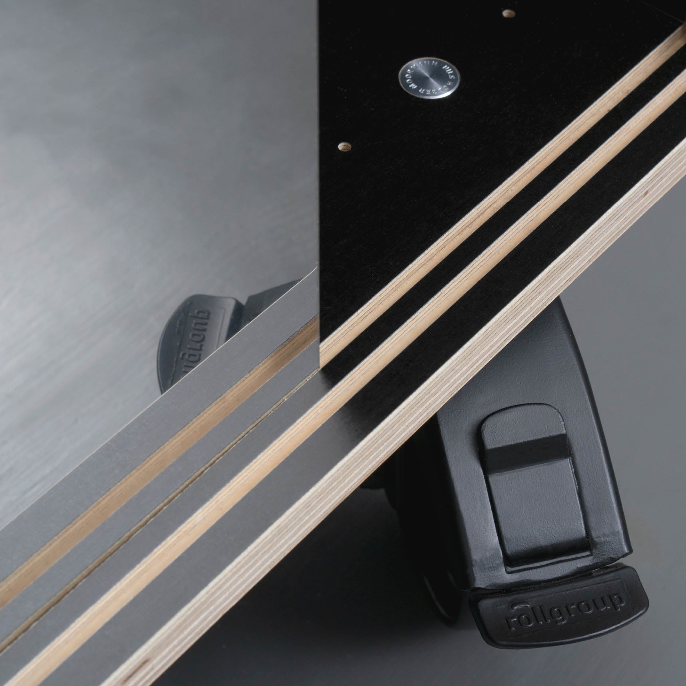 Close-up of Moormanns Egal Rockboard, a geometric piece featuring layered wooden panels and a black metal fixture. A triangular design is accentuated by a visible stainless steel screw against a smooth grey background, exuding modern elegance found in sideboards.