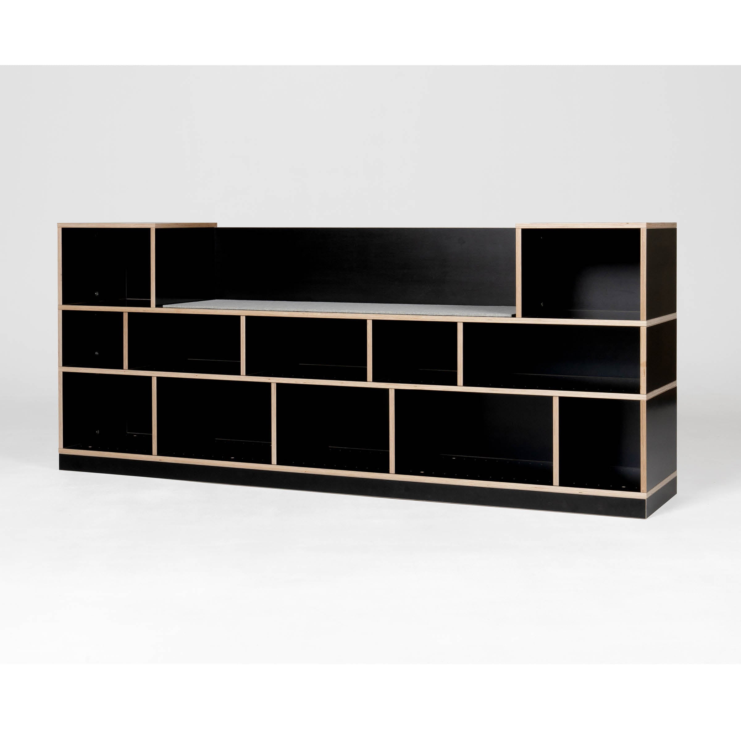 The Egal Sitzboard by Moormann is a sleek black modular shelving unit with customizable compartments in a staggered layout, highlighted by a plain white backdrop and light wood edges, elegantly transforming into a versatile sideboard.