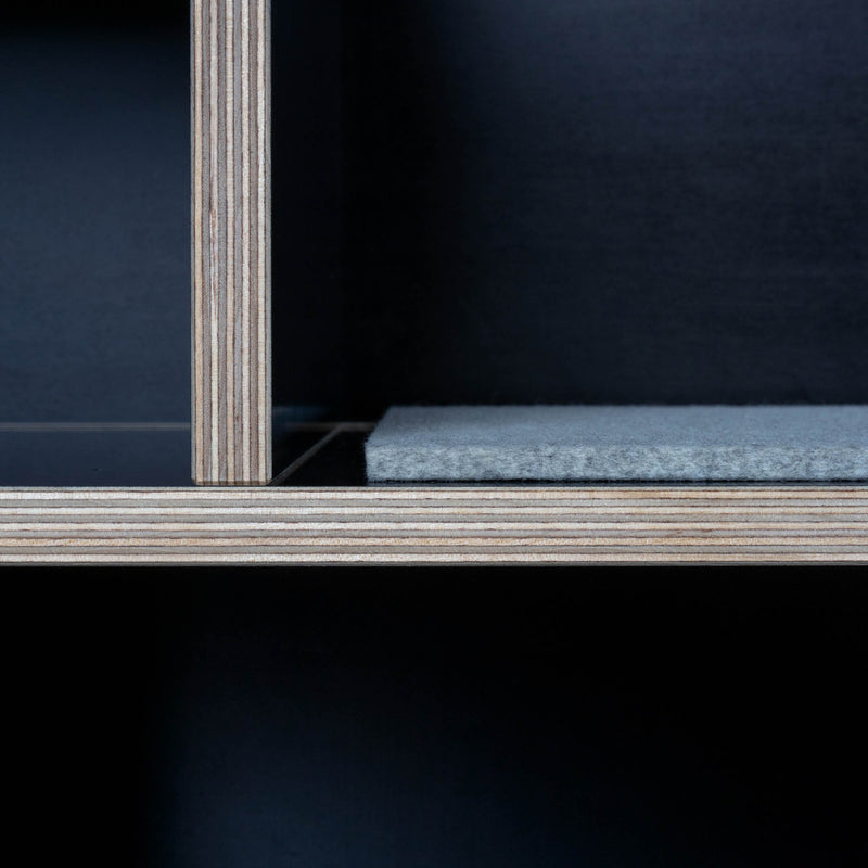 The Egal Sitzboard by Moormann is a sleek shelving unit made of layered wood, with visible edges. It features a dark upper compartment and felt-lined lower section, enhanced by customizable sliding doors for subtle texture contrast.