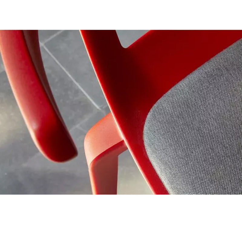 A close-up of the Resol Tokyo Chair Upholstered, featuring a red wooden frame with a grey cushioned seat, is set on dark tiles. Crafted sustainably, diagonal lighting highlights part of the backrest and creates soft shadows.