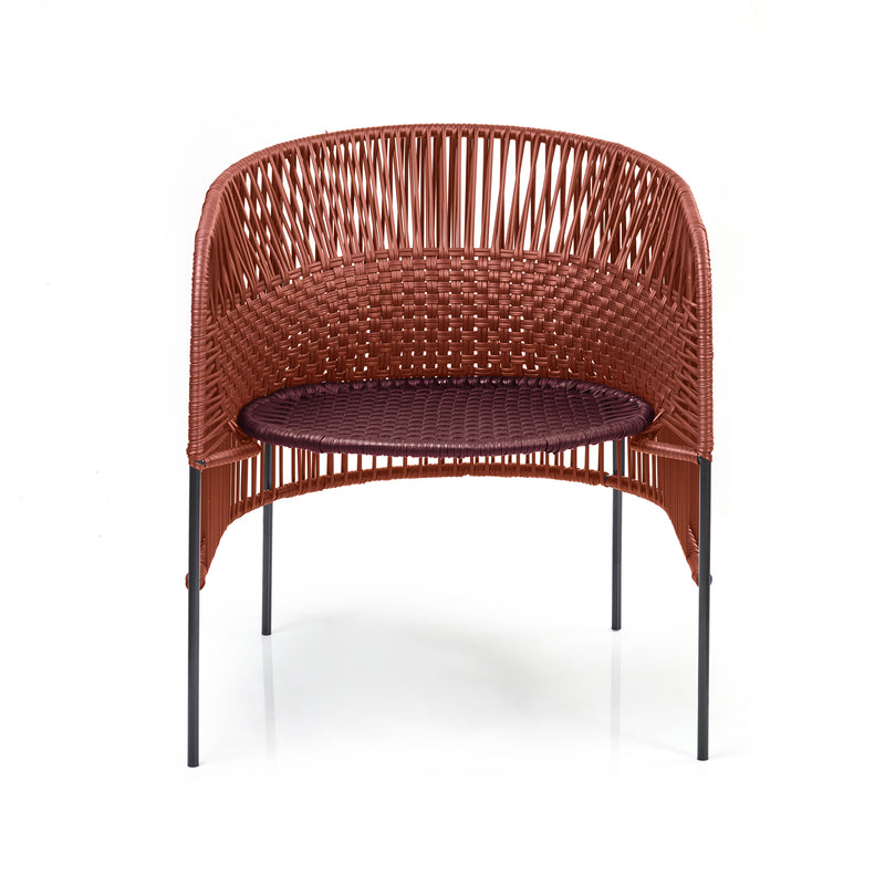 The Ames Caribe Chic Lounge Chair by Ames, designed by Sebastian Herkner, features a woven reddish-brown backrest and seat inspired by Colombian craft, with four slender black metal legs, set against a white background.