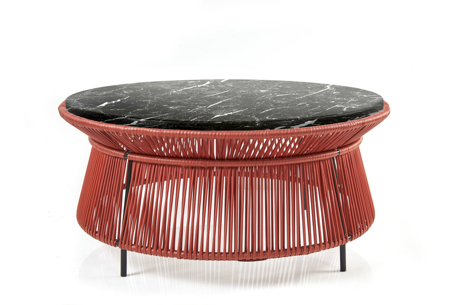 The Ames Caribe Chic Low Table by Ames, designed by Sebastian Herkner, features a black marble top and a red woven base with vertical and diagonal strands for an open, airy look against a white background.