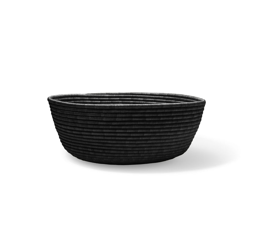 The Ames La Che Basket by Ames is a handmade, round black basket crafted from Fique fibers with a ribbed, textured surface, shown on a white background with a soft shadow.