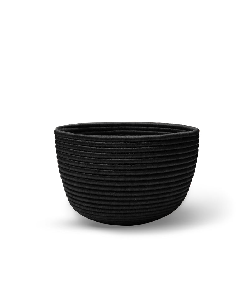 The Ames La Che Basket by Ames is a black, round bowl with a ribbed, textured exterior inspired by handmade Fique fiber baskets, shown on a white background.