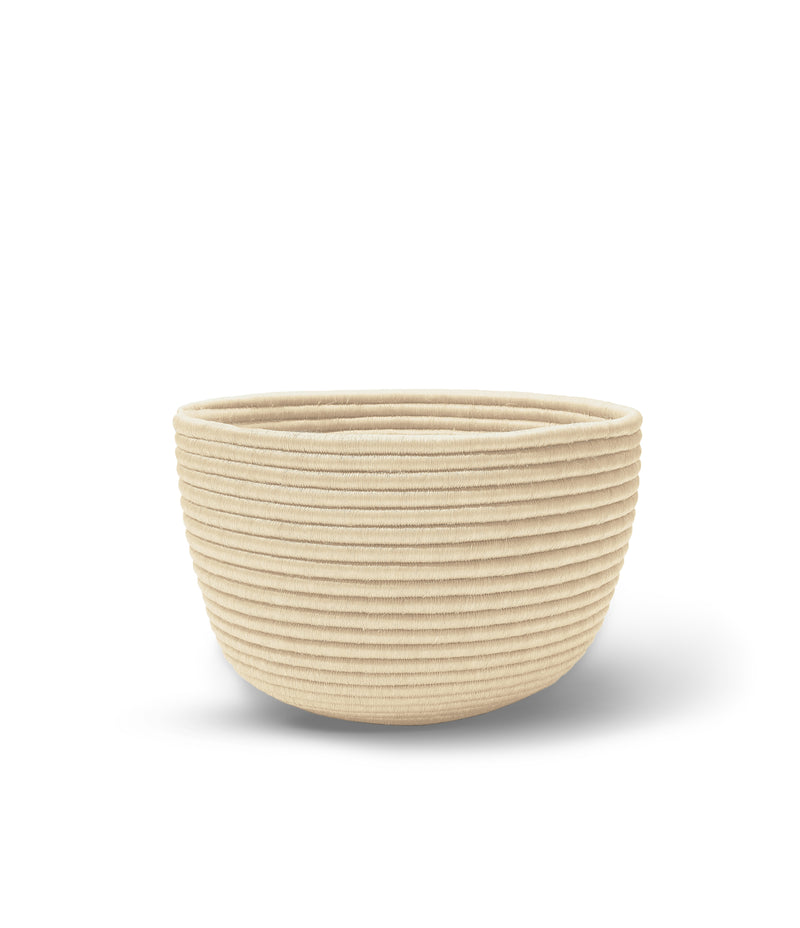 The Ames La Che Basket by Ames is a round, beige woven basket crafted from natural fique fibers. Its ribbed texture and subtle shadow on a white background highlight the handmade charm of this stylish home accessory.