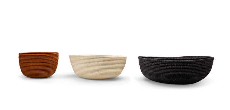 Three Ames La Che Baskets by Ames, handmade in varying sizes and brown, beige, and black colors from durable Fique fibers, are arranged side by side on a white background.