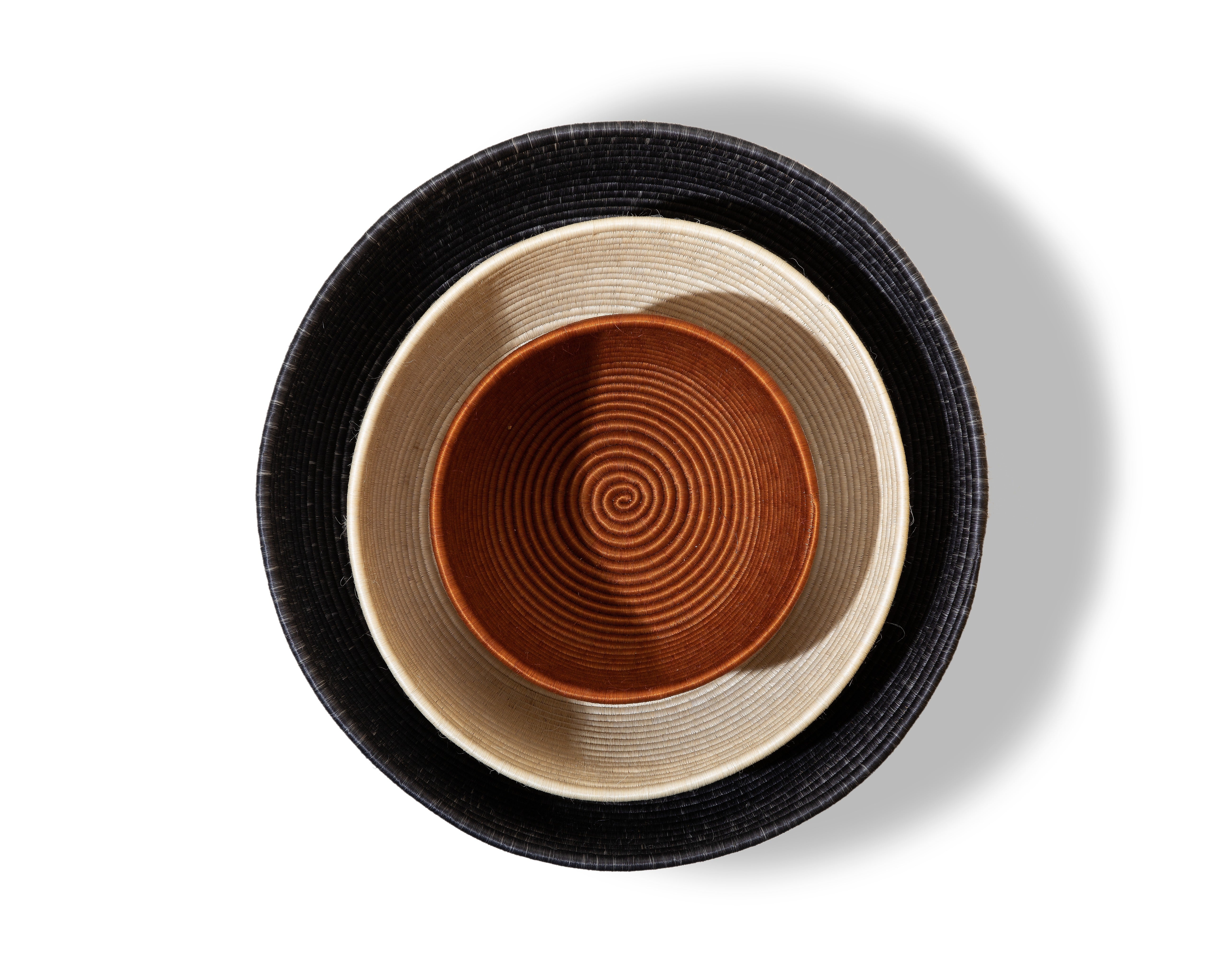 The Ames La Che Baskets by Ames feature three concentric handmade baskets in black, beige, and brown, crafted from natural Fique fibers and stacked together on a white background with shadows to the right.