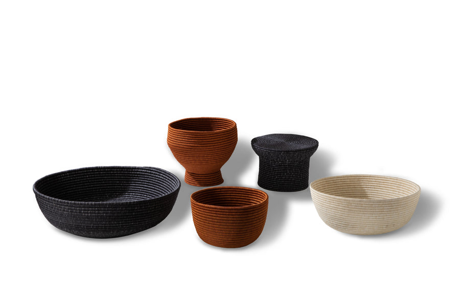 Five Ames La Che Baskets by Ames, handcrafted from fique fibers in black, rust, and cream tones, are displayed in various shapes and sizes against a white background.