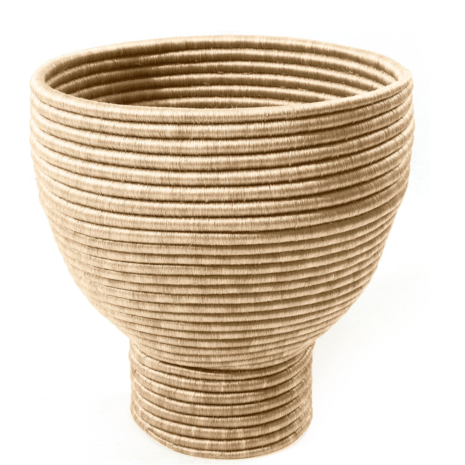 The Ames La Che Pot by Ames is a large, round, tan fique fiber bowl with a textured coiled rope design—wider at the top and narrowing at the base—reflecting Colombian culture, set against a white background.