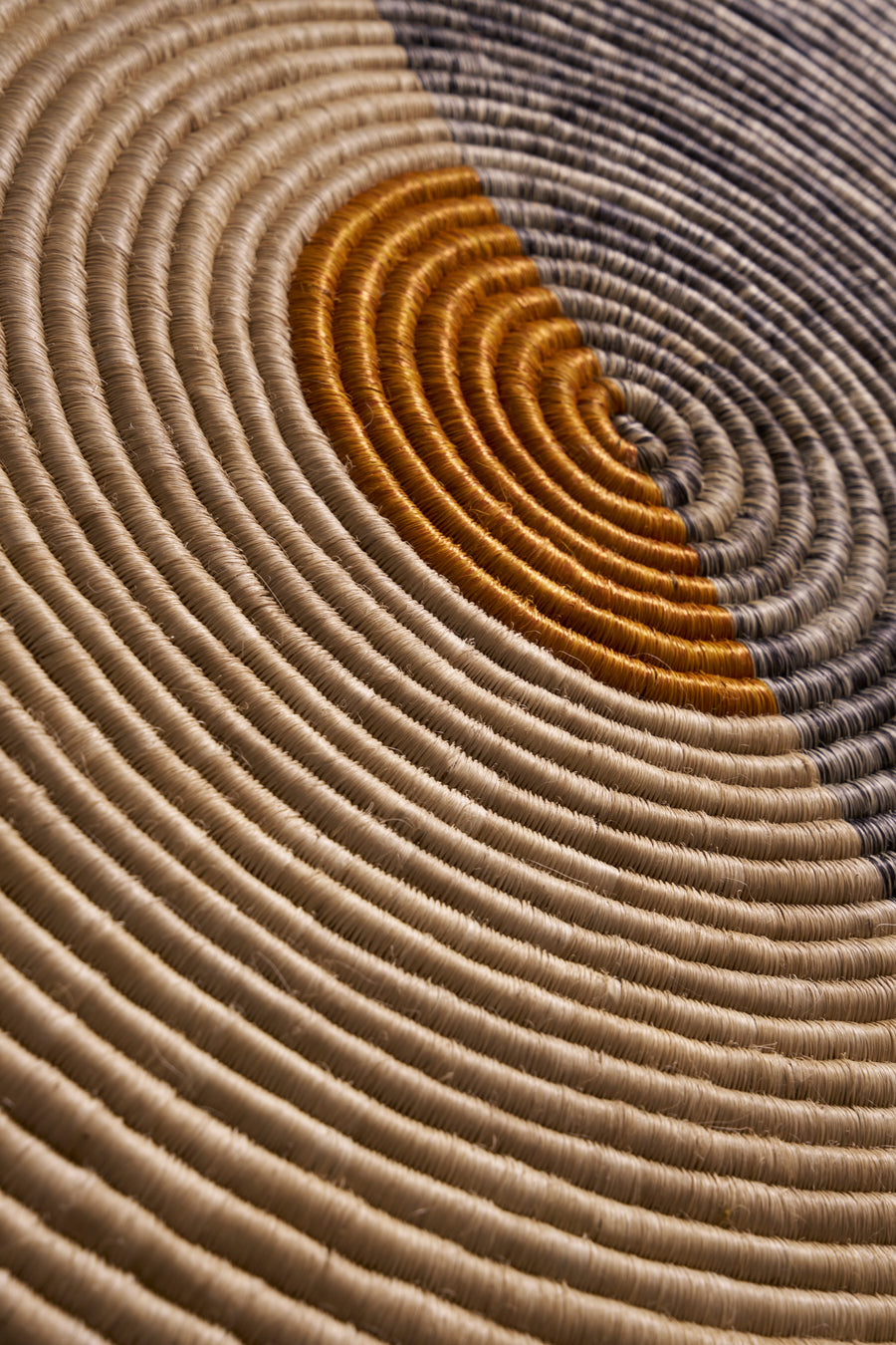 Close-up of the Ames Ojitos Wall Decoration Andes by Ames, featuring concentric circles in beige, mustard yellow, and gray—expertly crafted from tightly coiled fique palm fibers with a rich textured finish.