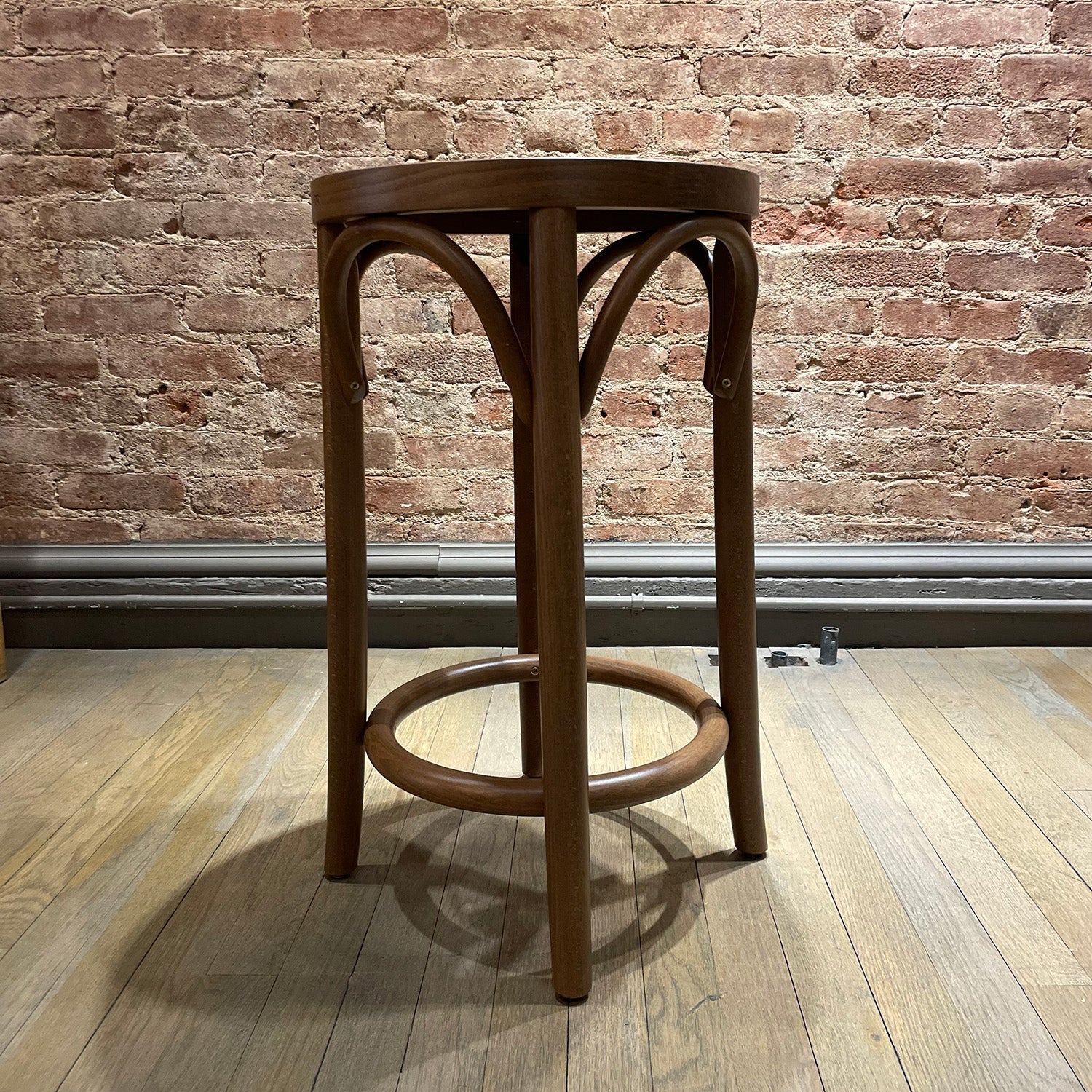 A TON Barstool 73 with beech leg joints and a round seat sits on a light wooden floor, set against an exposed brick wall.