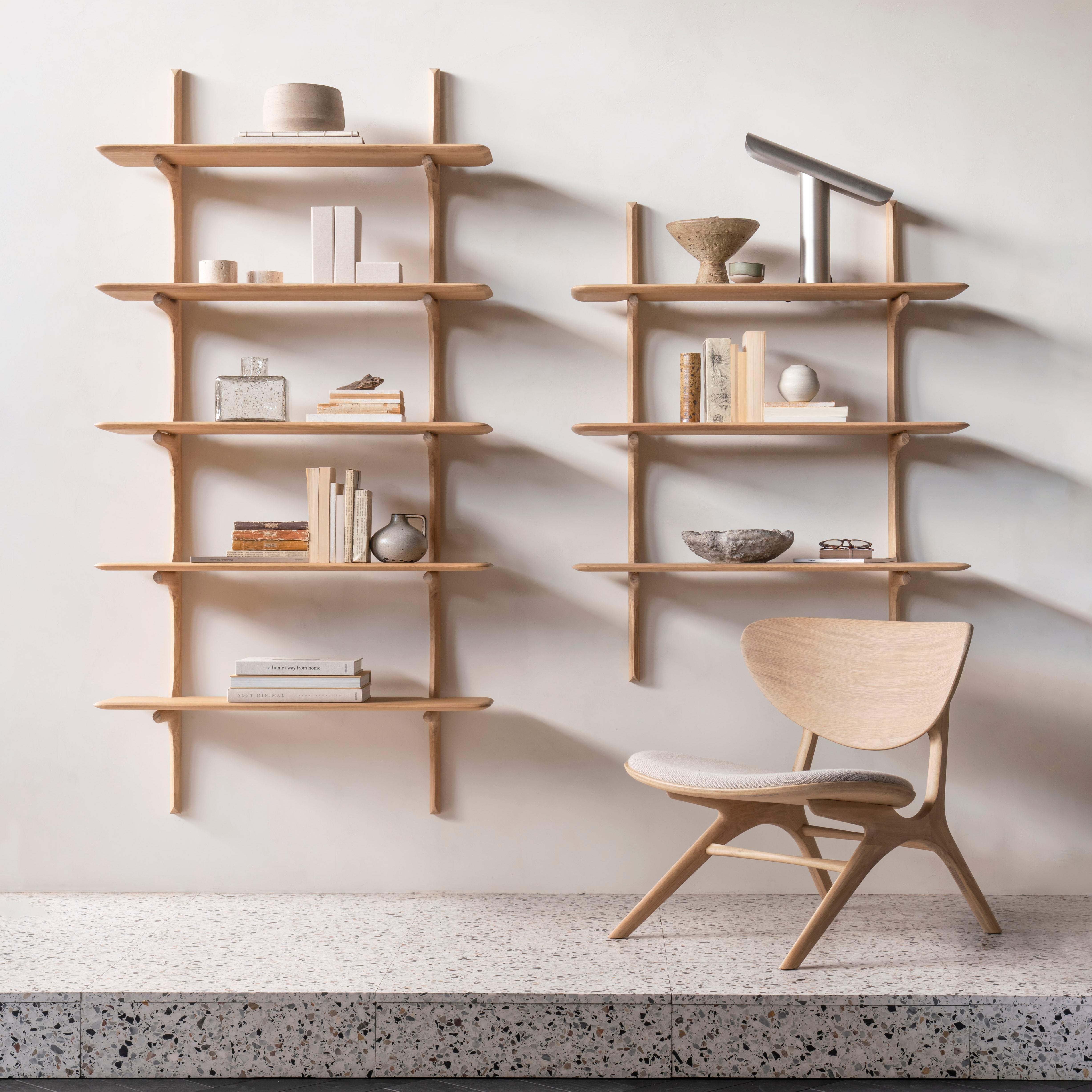 Eye Lounge Chair in light wood with off-white fabric seat, beside minimalist wooden wall shelves with books and decor.