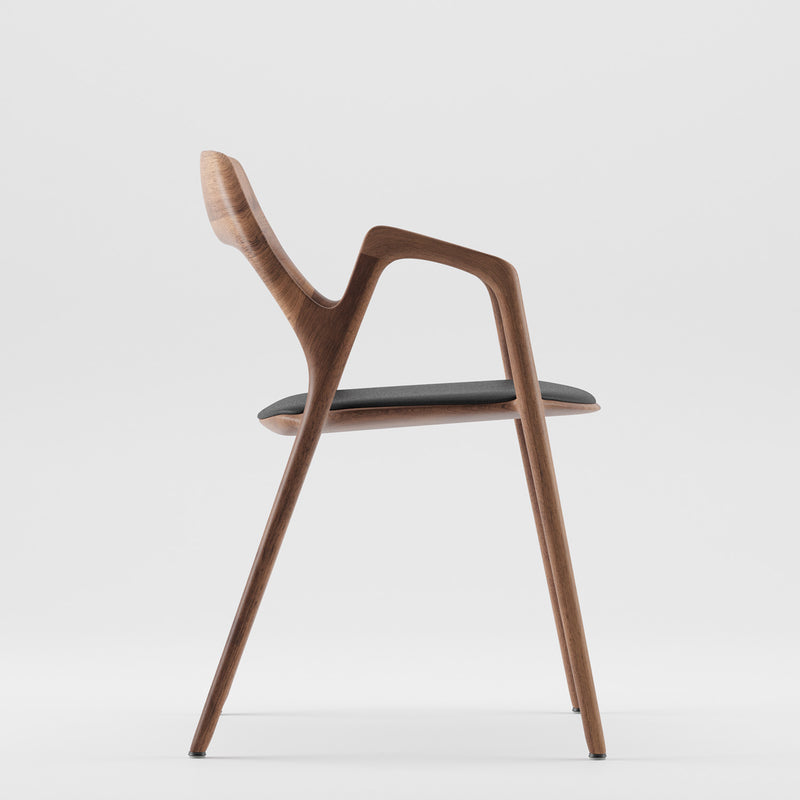 Side view of the Ging Chair by Artisan, a modern minimalist design in solid wood with a curved backrest and black cushioned seat, elegantly showcased against a white background.