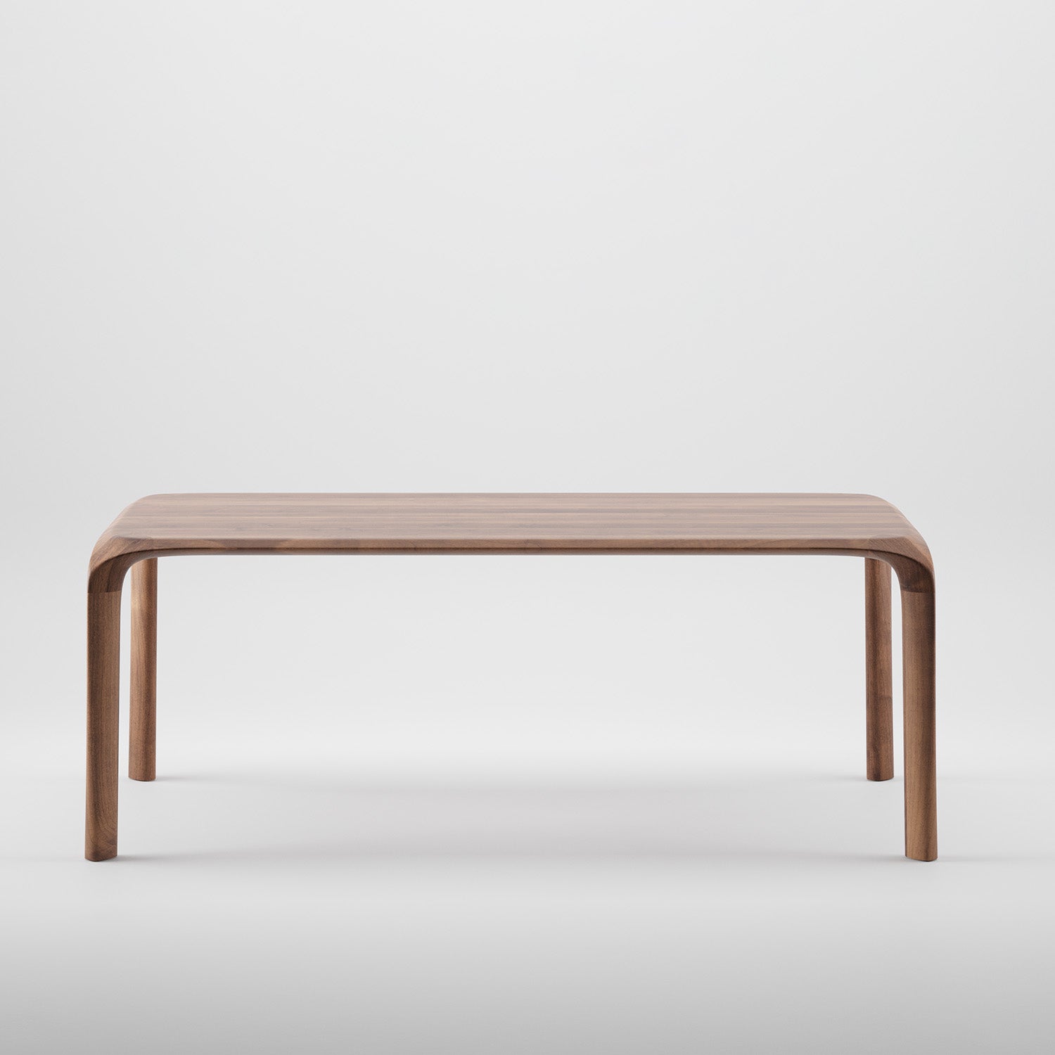 The Ging Table by Artisan features a simple, modern design crafted from solid wood with a smooth light brown finish and curved edges, highlighting the organic beauty of wood. It stands gracefully on four legs against a plain white background.