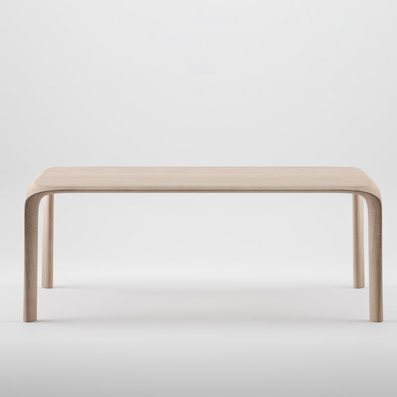 The Artisan Ging Table is a minimalist, solid wood table featuring gently curved legs and a smooth, light finish. Set against a plain white background, it highlights the organic beauty and simple elegance of its design.