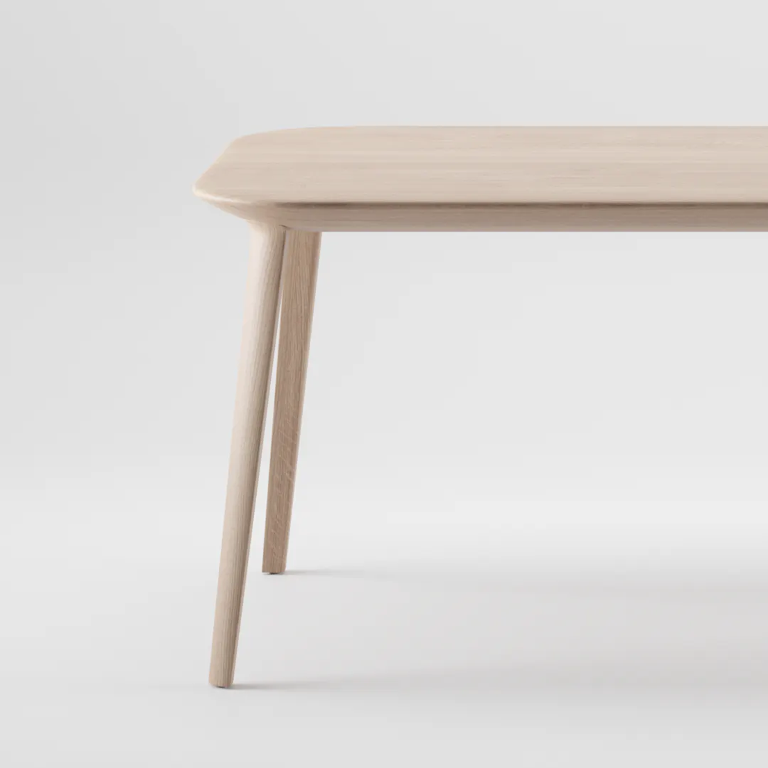 The KALOTA Table by Artisan is a minimalist wooden table with a smooth, light finish and natural oils. It features rounded edges, four angled legs, and its simple yet elegant design is showcased against a plain white background from a corner view.