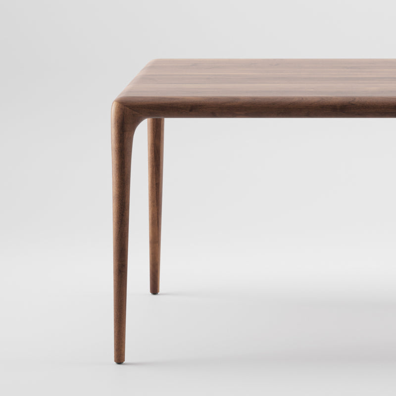 The LATUS Table by Artisan is a solid wood piece with a minimalist design featuring slender, tapered legs. Its smooth surface boasts a rich natural wood grain finish enhanced by eco-friendly materials, highlighted against a plain white background to showcase its elegant simplicity.