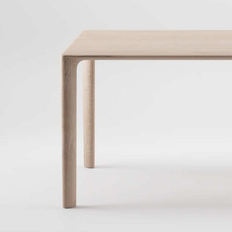 The MELA Table by Artisan is a minimalist piece crafted from solid wood with a light finish. A close-up against a white background highlights its simple design and smooth texture, enhanced by natural oils.