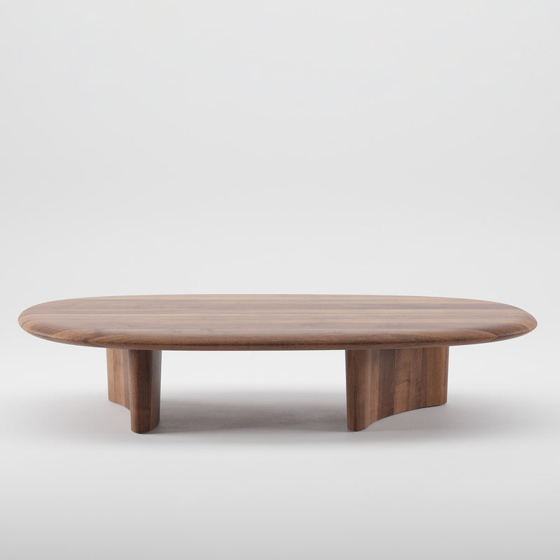 The Artisan MONUMENT Oval Coffeetable is a sleek, solid wood table with a smooth surface and rounded edges. Its minimalist design features two sturdy legs and a natural wood finish enhanced by eco-friendly oils, all set against a plain white background.