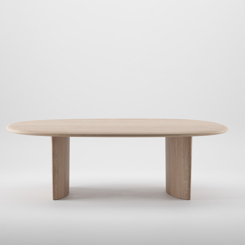 The MONUMENT Oval Table by Artisan is a minimalist wooden table crafted from solid wood, featuring an oval top and two curved legs. Its light finish, achieved with natural oils, gives it a modern touch. Placed against a plain white background, its eco-friendly appeal is enhanced.