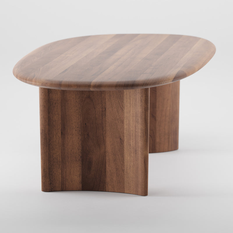 The MONUMENT Table by Artisan is a small, low table made from solid wood, featuring a polished finish with a rounded rectangular top and curved legs on a white background.