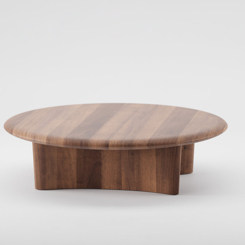 The Artisan MONUMENT Round Coffeetable is crafted from solid wood with a smooth, polished finish. Made using eco-friendly materials and natural oils, its rich brown hue showcases stunning grain patterns, elegantly set against a light gray background.