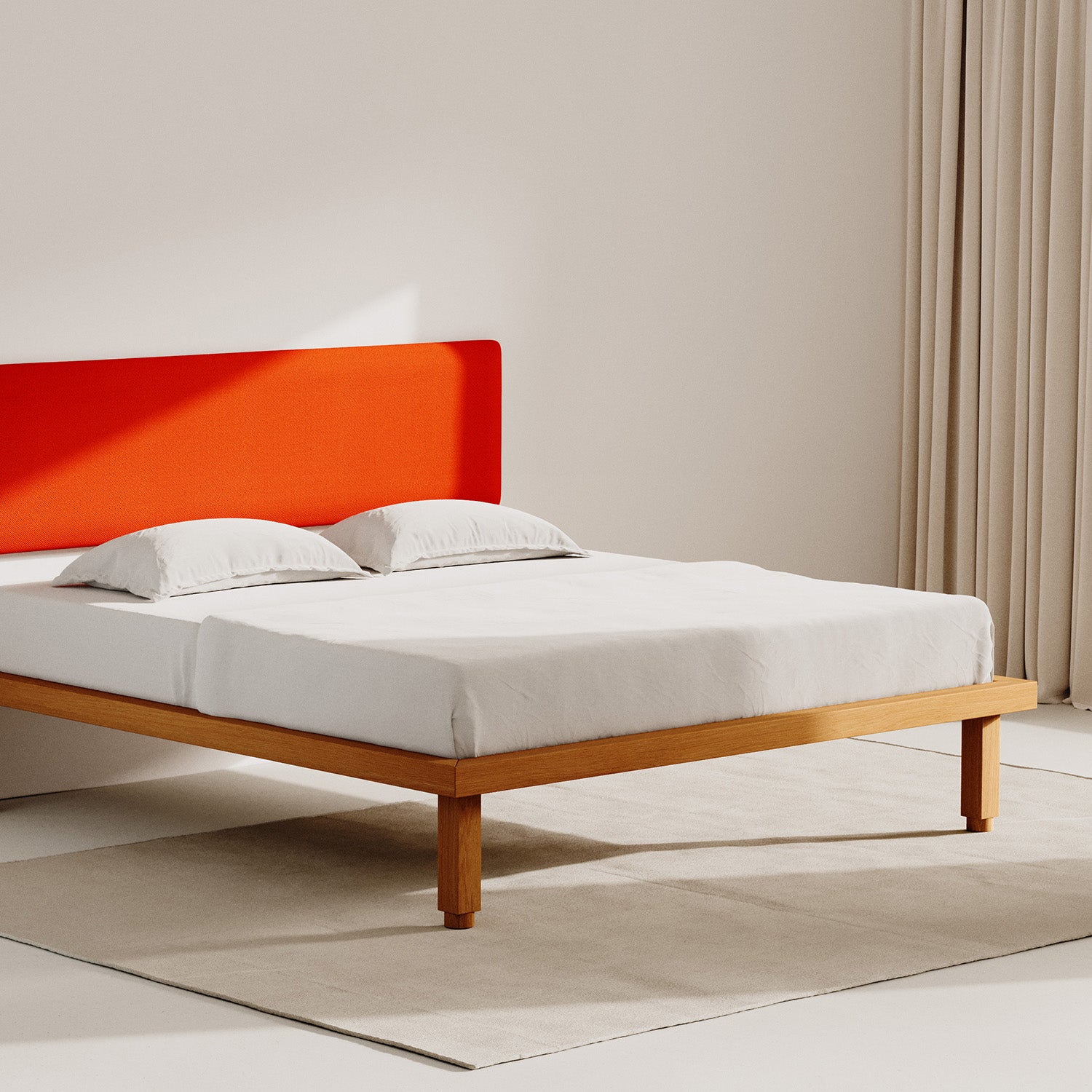 A cozy bedroom with a minimalist vibe showcases a wooden bed frame and the Frey Headboard from Objekte unserer Tage in bright orange. High-quality white bedding complements two pillows on a light rug, set against elegant beige curtains.