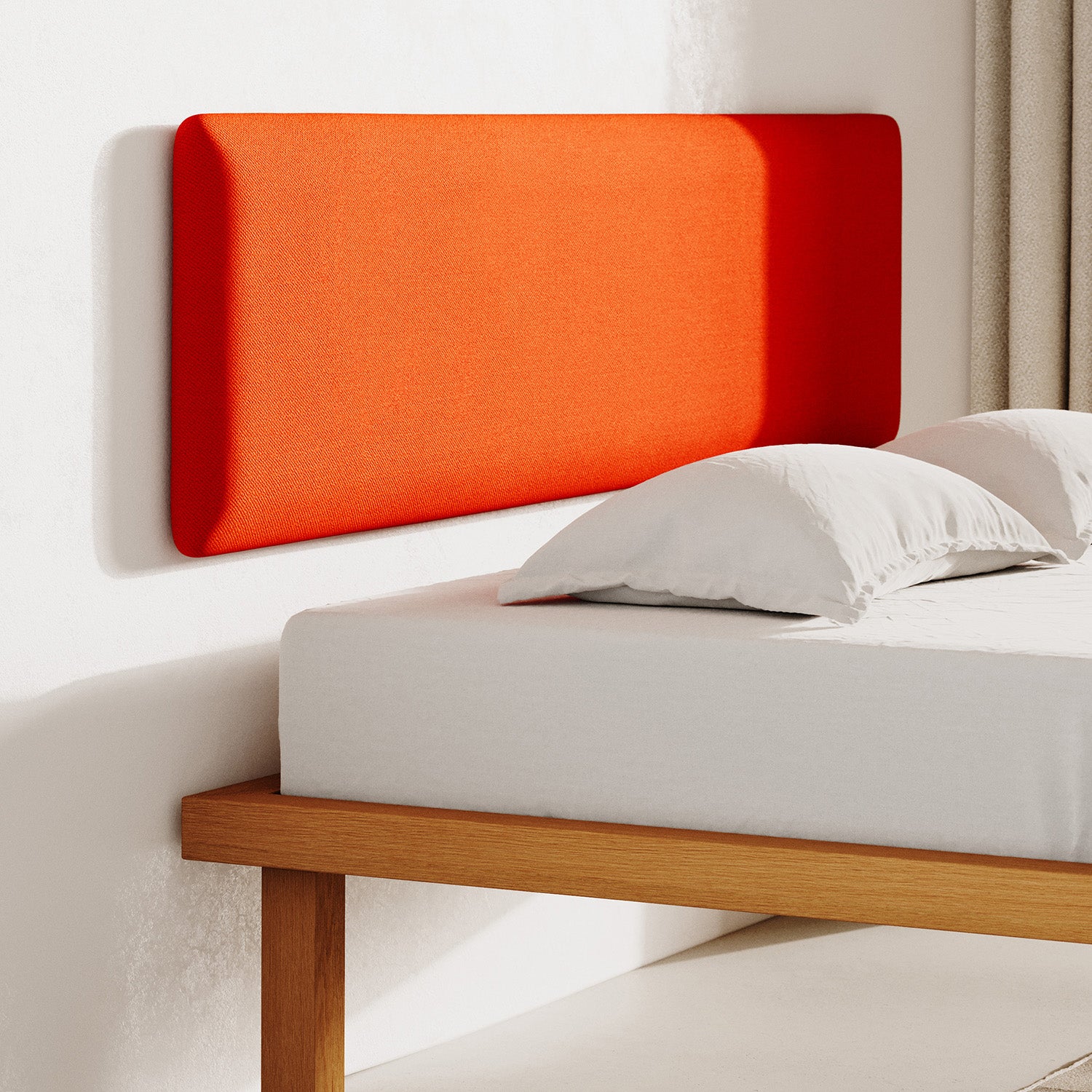 A minimalist bedroom features a wooden bed frame, white mattress, and pillows. Enhanced by an Objekte unserer Tage Frey Headboard in rich orange fabric, it adds warmth. Neutral tones complement the sunlight streaming through the window.