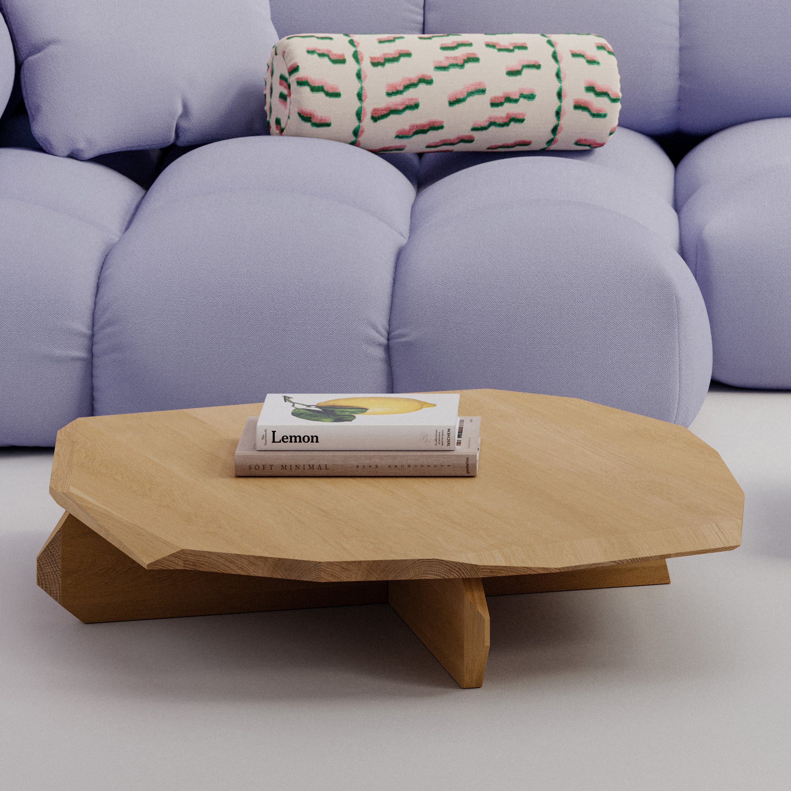 The Objekte unserer Tage Fels Coffee Table with a geometric wooden design holds two books, including Lemon, and sits in front of a light purple couch with rounded cushions. A rolled pillow featuring a white cover with green and pink patterns enhances the sculptural aesthetics.
