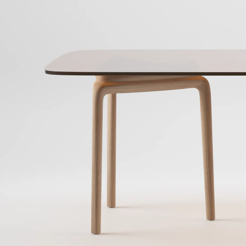 The PASCAL Rectangular Table by Artisan boasts a sleek, dark surface with rounded edges and is supported by a light wood frame made from eco-friendly materials, complete with curved legs. It stands against a plain white background, emphasizing its modern and minimalist design.