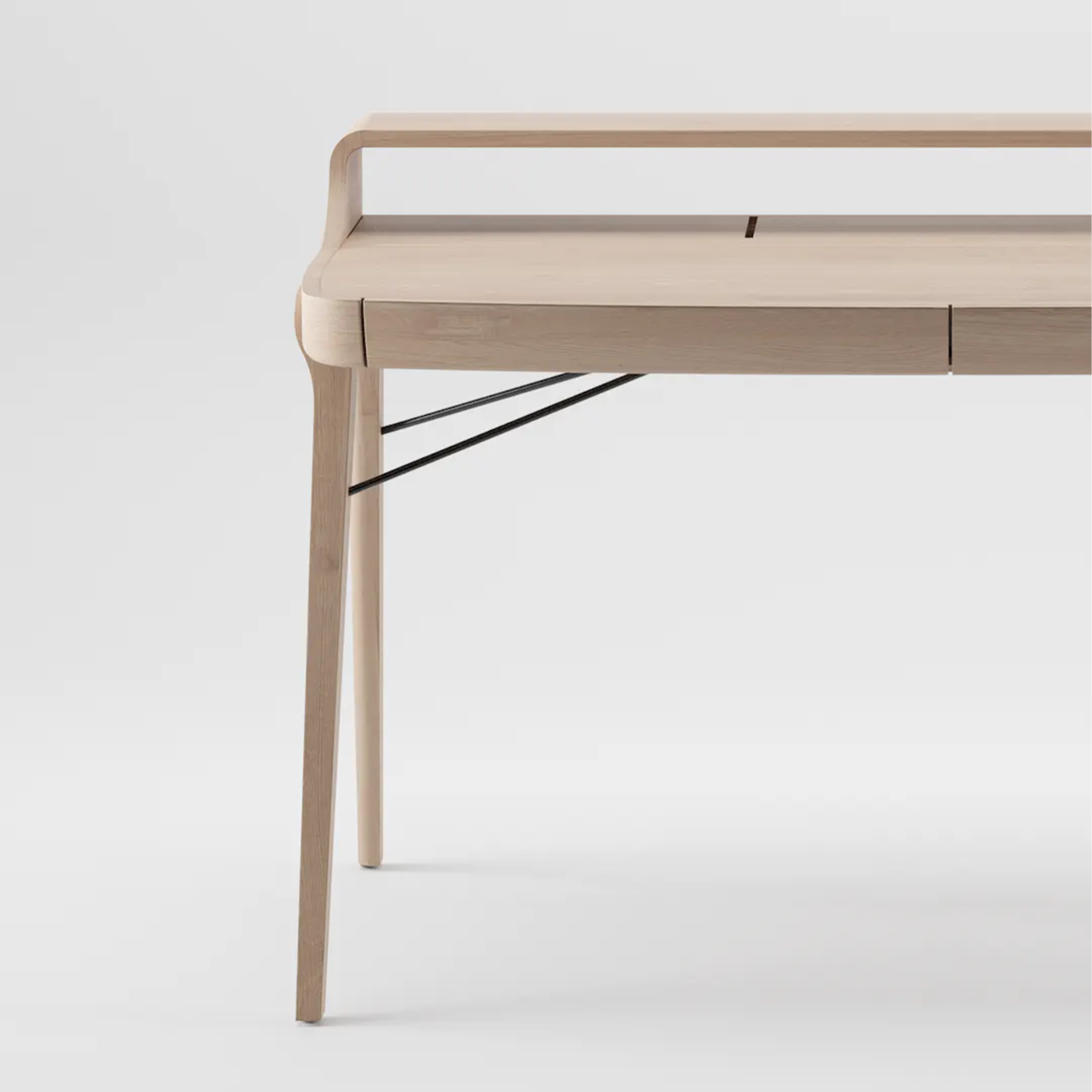 The PICARD Desk by Artisan is a minimalist solid wood table with sleek lines, featuring four light-colored legs, a raised back edge, and metal support rods. Its modern design is elegantly showcased against a plain white background.