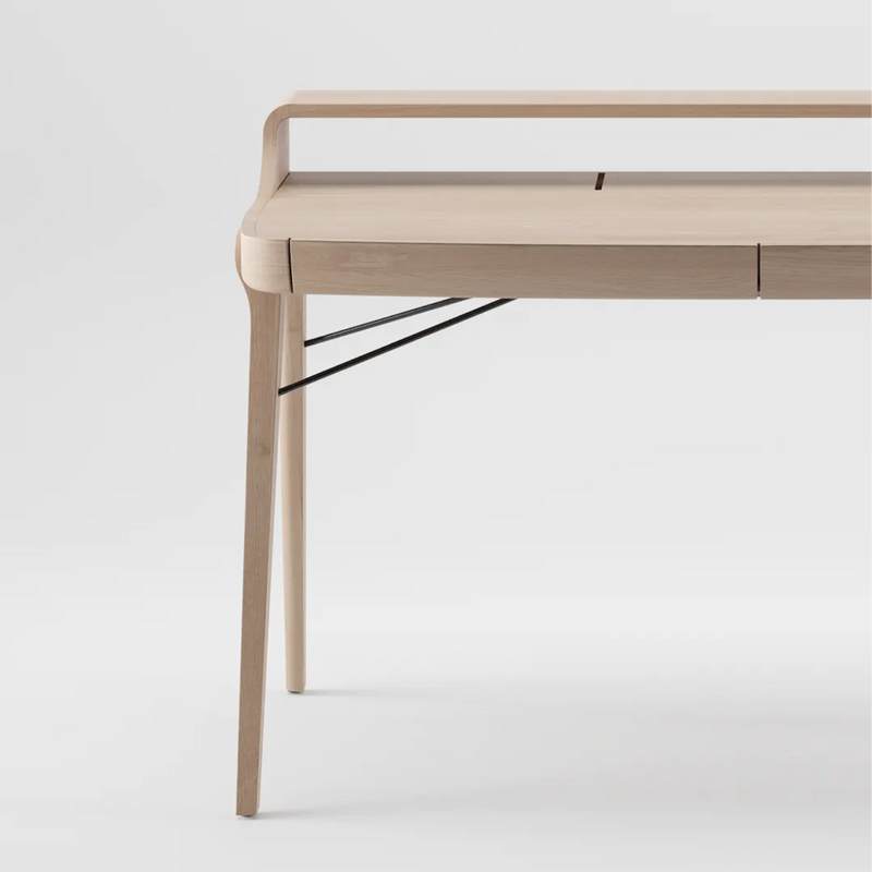 The PICARD Desk by Artisan is a minimalist solid wood table with sleek lines, featuring four light-colored legs, a raised back edge, and metal support rods. Its modern design is elegantly showcased against a plain white background.