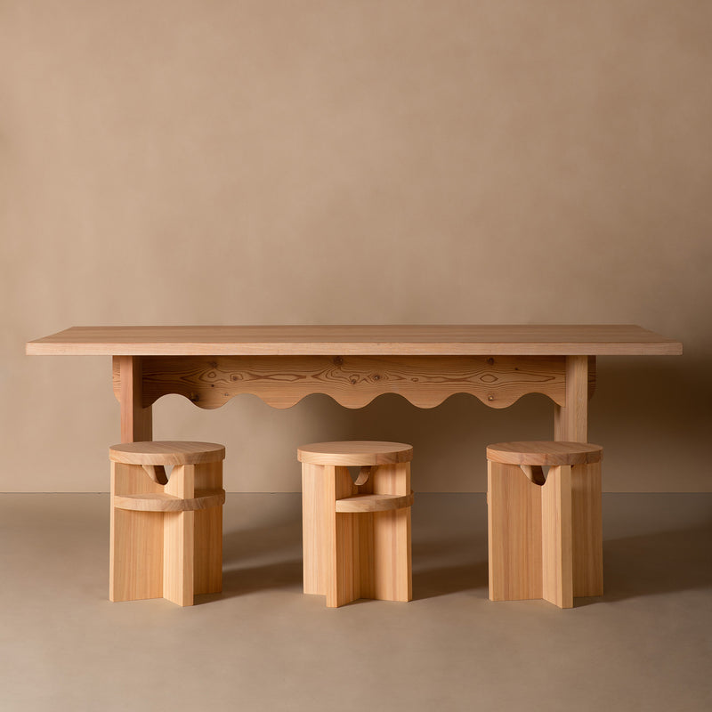 The Schneid Tami Dining Collection features a minimalist wooden table with wavy edges and three matching Tami Stools made from naturally oiled larch wood, showcasing geometric cutouts on a neutral beige background for a cohesive, natural look.