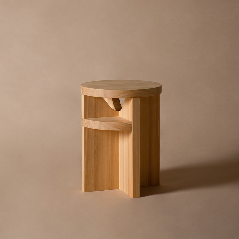 The Schneid Tami Stool, made from naturally oiled larch wood, showcases a round seat and interlocking geometric base. Positioned against a beige backdrop, it perfectly complements the refined style of the Tami Dining Collection.