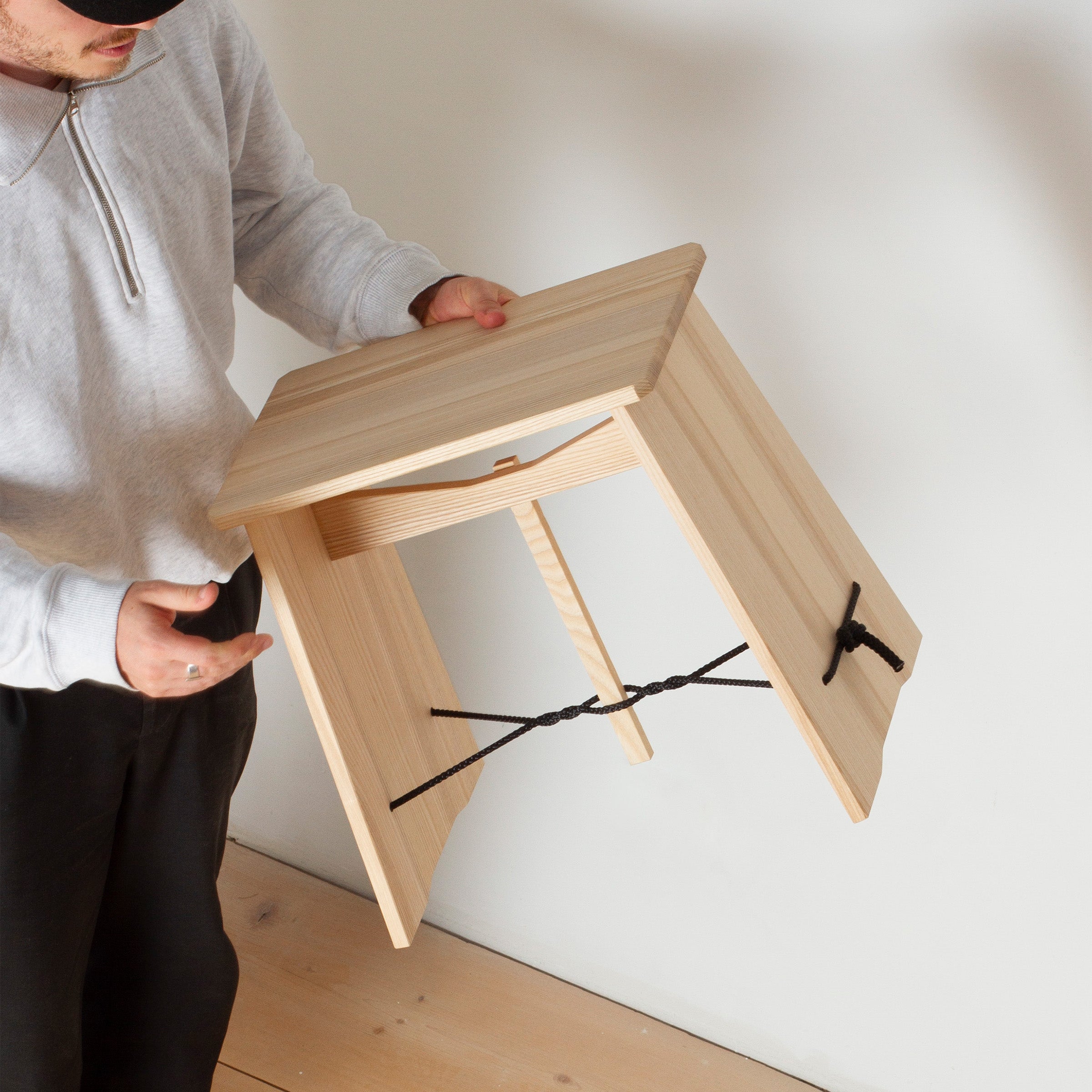 Person holding a light wood Strammer Max stool made of birch plywood with twisted cord binding.