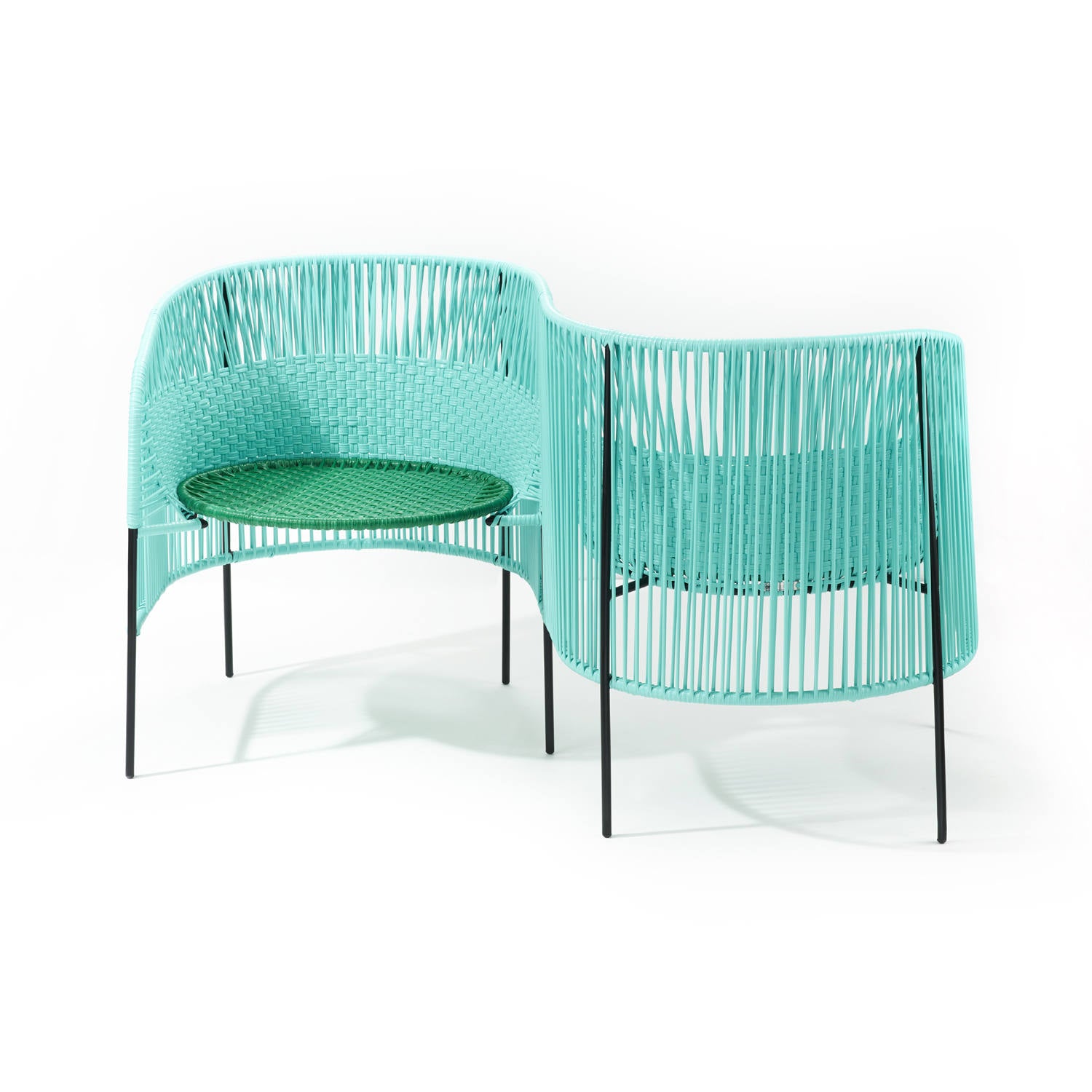 The Caribe Double Chair - Sale by Ames features interconnected chairs with turquoise Momposino weave backs and dark legs. Each seat boasts a complementary green cushion, reflecting the modern style of Sebastian Herkners designs, forming an L-shaped chic corner seating arrangement.
