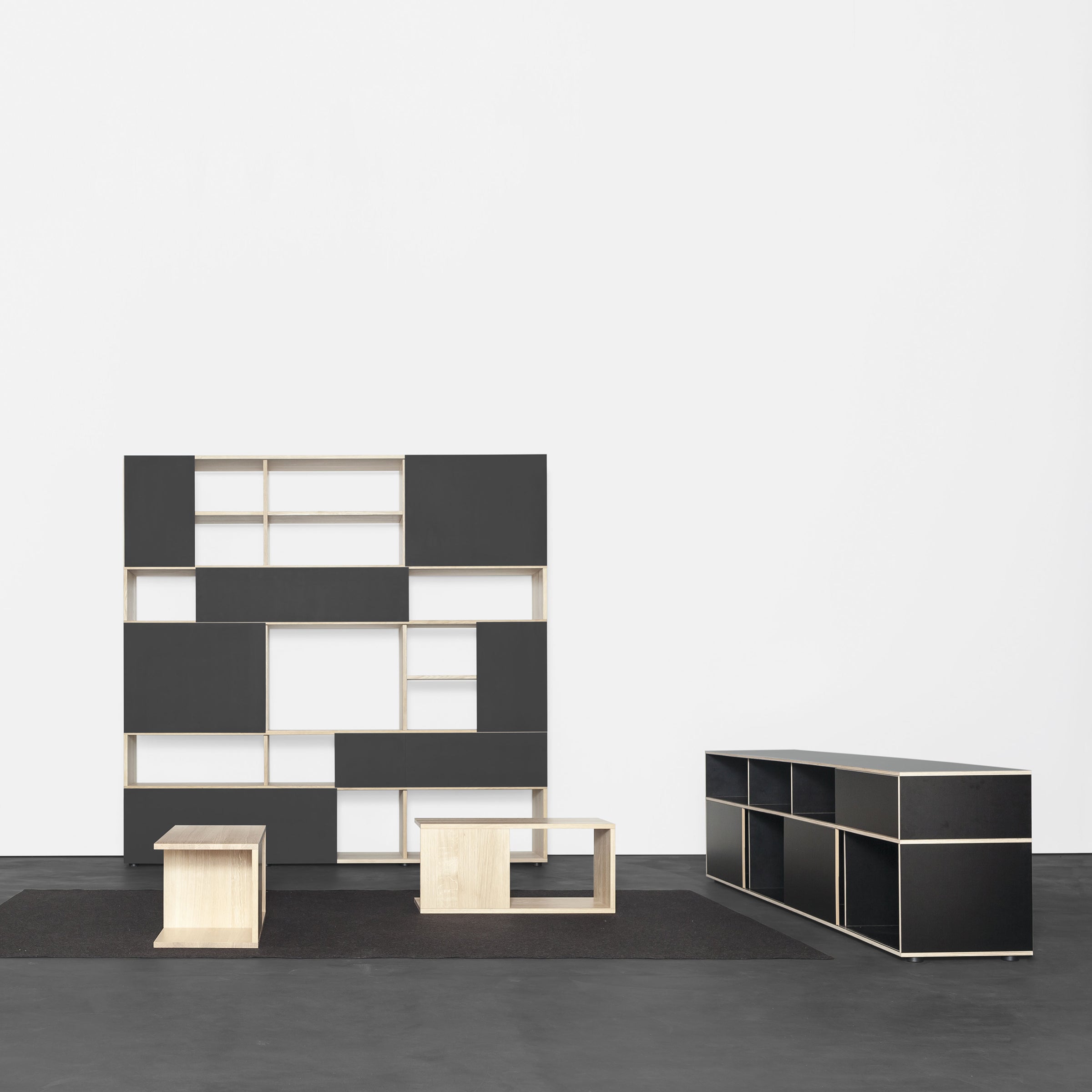 The Sanktjohanser Basic Multipurpose set features black and beige modular furniture on a dark floor, with a large geometric shelving unit, rectangular sideboard, and two cube tables, all against a plain white wall.