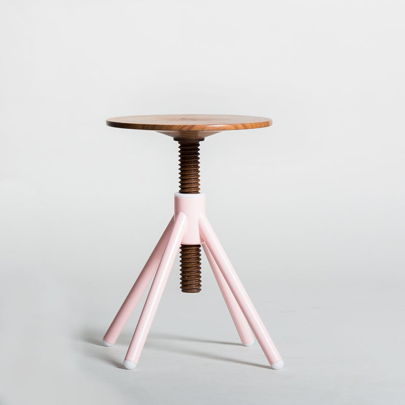 The Thread Family Stool by Coordination Berlin is crafted from walnut wood, featuring a round seat and a pink, three-legged base. Its screw-like metal support allows height adjustment, combining functionality and style against a plain white background.