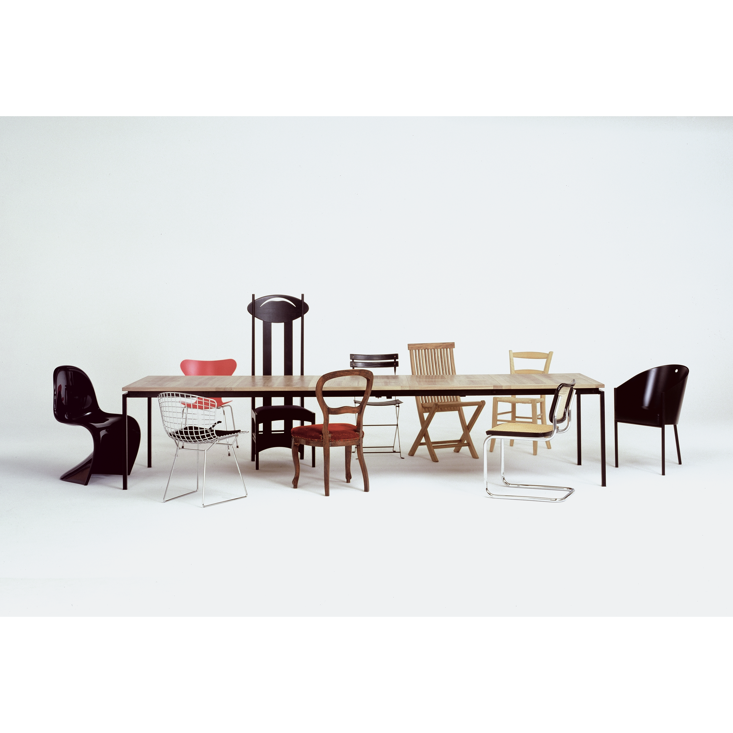 The UPW 1010 Extendable Table by WB Form is encircled by an eclectic array of chairs, each demonstrating exceptional craftsmanship. Featuring diverse materials, colors, and designs, these chairs form an artistic ensemble against a plain white backdrop.