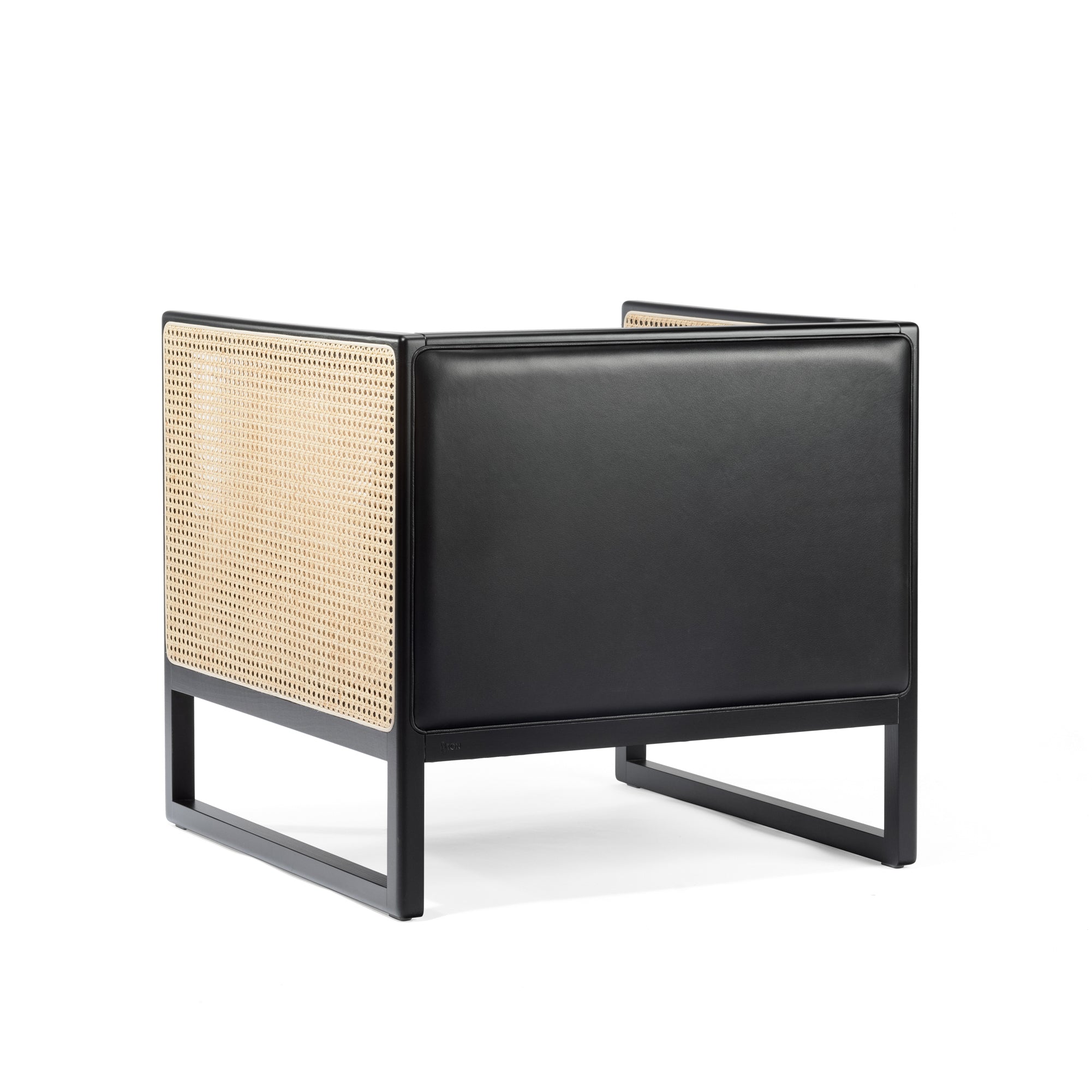 The Armchair Casablanca by TON is a modern black lounge chair with sleek edges, featuring light tan rattan weaving on the back and sides. Its seat and front are upholstered in smooth black leather, while stylish cane weave armrests add an elegant touch to its minimalist design.