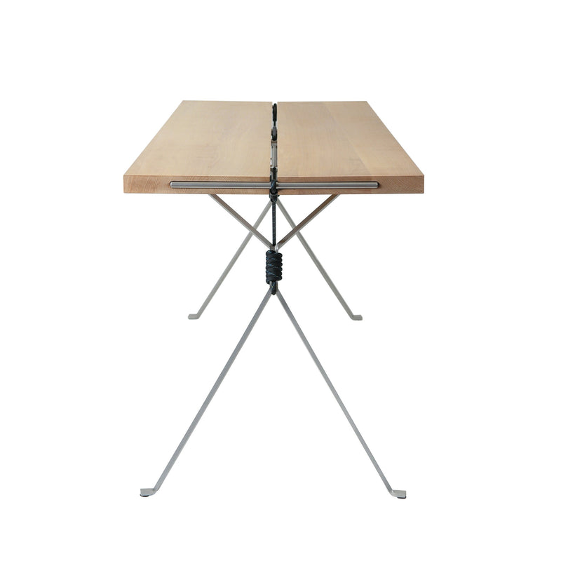 Introducing the Kampenwand Table by Moormann, a minimalist piece with a rectangular wooden top and slender metal base. Its X-shaped design features a striking black coil at the center, perfectly set against a plain white backdrop.