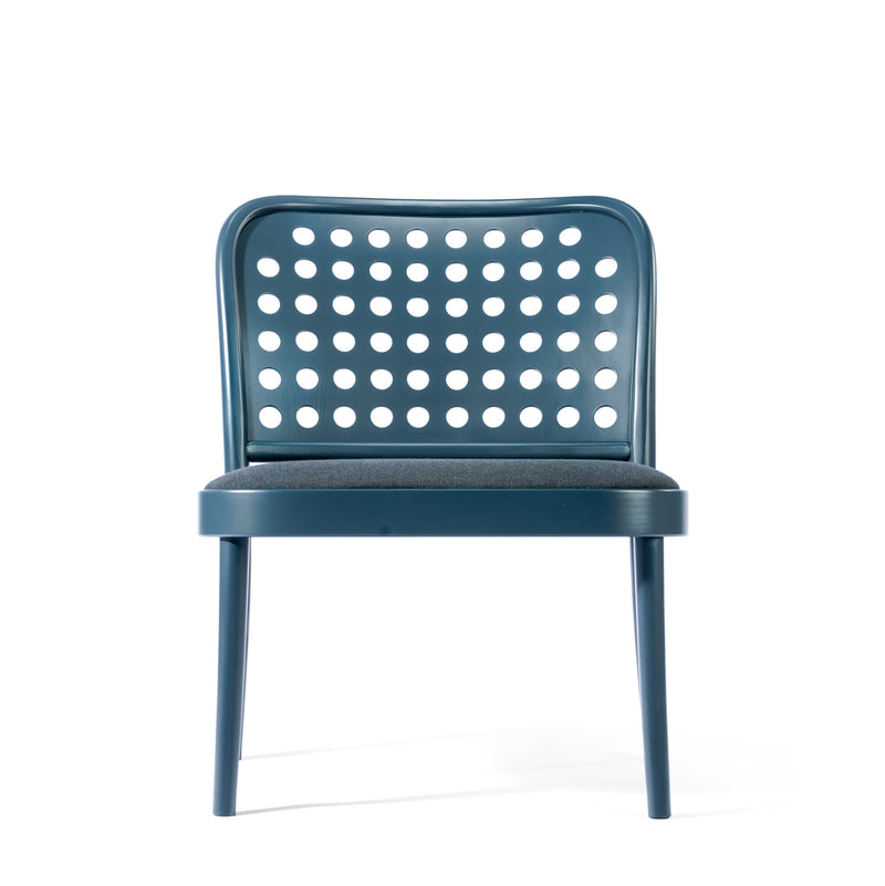 The Lounge Chair 822 by TON, inspired by Scandinavian minimalism, is a modern blue chair with a rounded perforated backrest featuring circular holes and a cushioned seat supported by four straight legs, beautifully captured against a white background.
