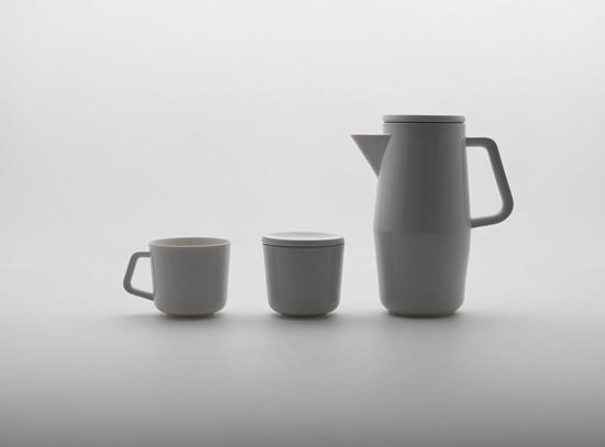 The Augarten Orbit Collection features a minimalist trio of white ceramic pieces: a small cup with a semi-matt polished rim, a lidded container, and a tall pitcher with handle and spout, elegantly displayed on a smooth white surface against a light gray background.