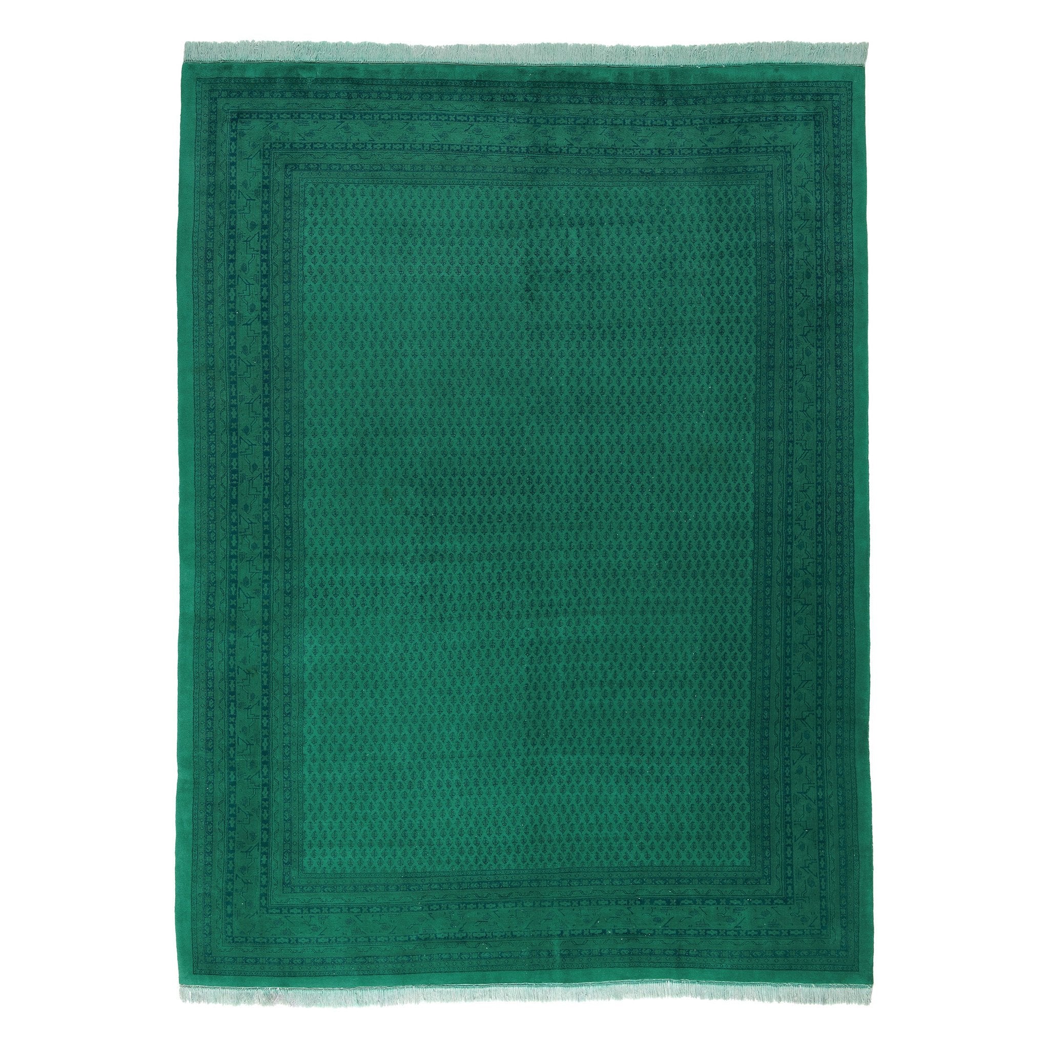 The Kiskan Color Carpet #92, a rectangular green rug made from 100% wool, features intricate dark green geometric patterns and decorative borders, drawing inspiration from the Indo Mir style. It has short white fringes on the shorter ends.