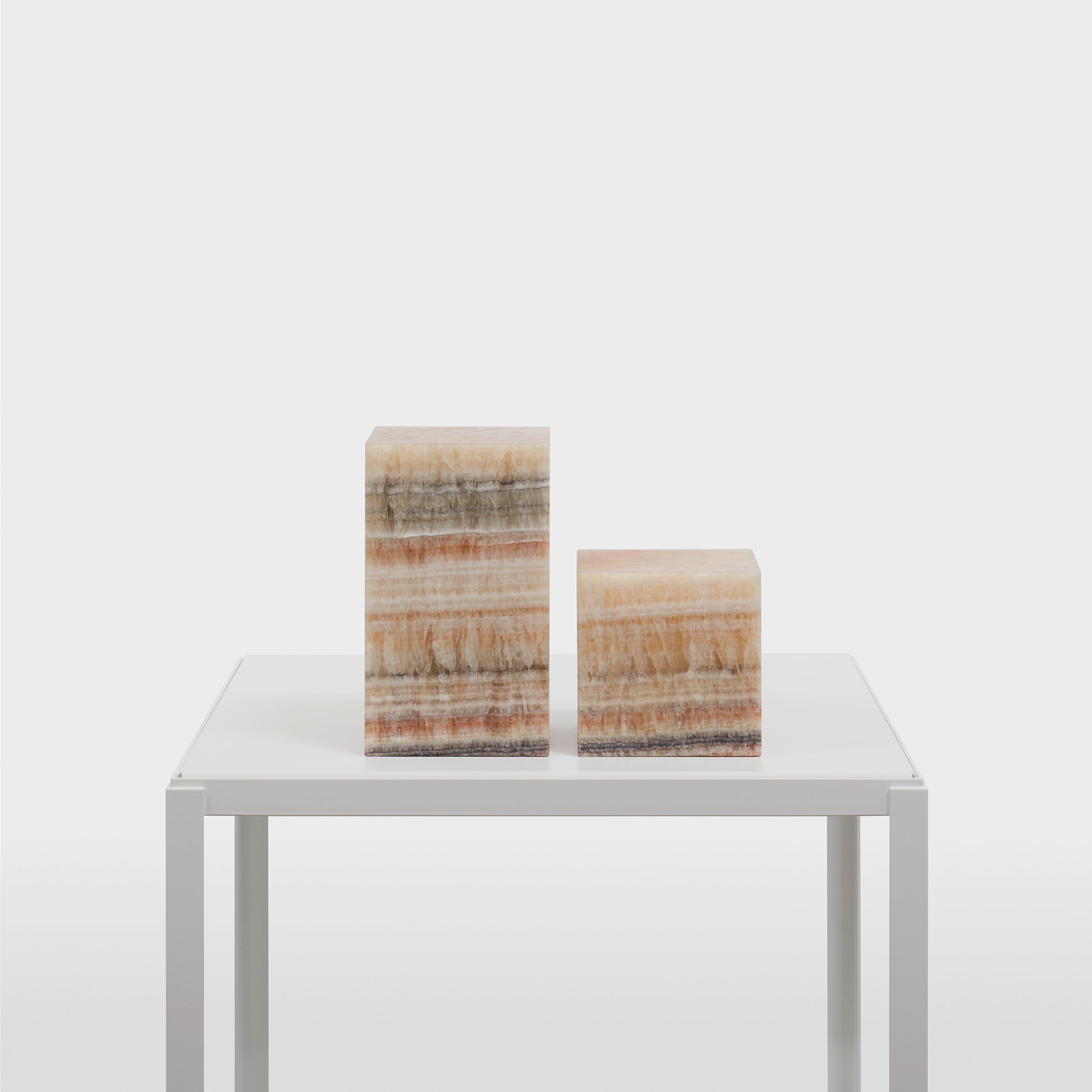 Two AC11 Stop Onyx rectangular sculptures in beige, brown, and gray stripes sit elegantly on a white minimalist table. From the E15 brand, these sculptural accessories add sophistication to the plain white background.